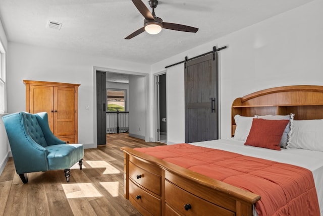 bedroom with a barn door, ceiling fan, and light hardwood / wood-style floors