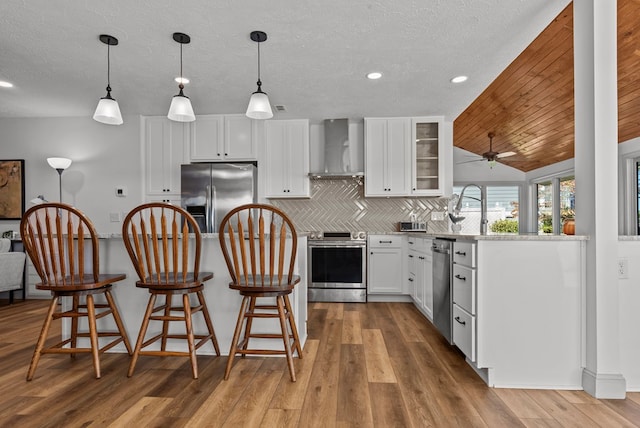 kitchen with white cabinetry, wall chimney exhaust hood, stainless steel appliances, tasteful backsplash, and pendant lighting