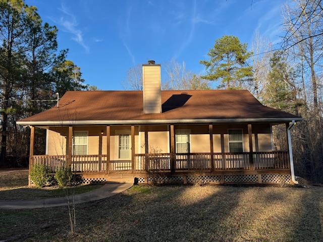 rear view of house with a porch, a yard, and a chimney