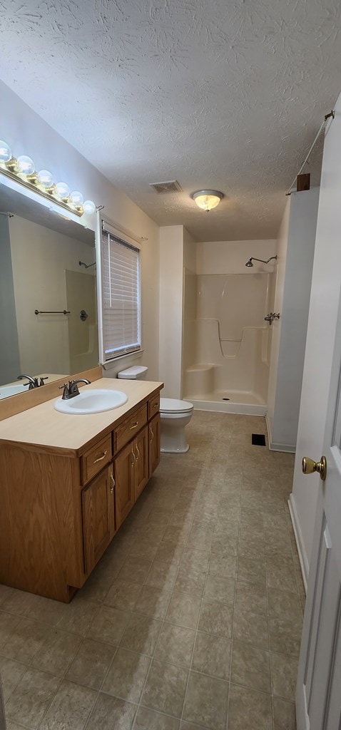 bathroom with visible vents, toilet, walk in shower, a textured ceiling, and vanity