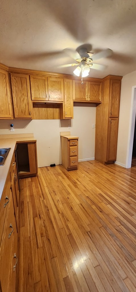 kitchen featuring light wood-style floors, ceiling fan, light countertops, and brown cabinetry