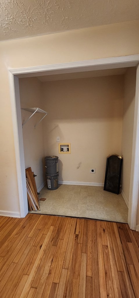 laundry area with laundry area, baseboards, light wood-style flooring, a textured ceiling, and washer hookup