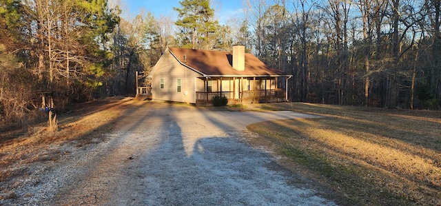 view of front of home with driveway, covered porch, a chimney, and a front lawn