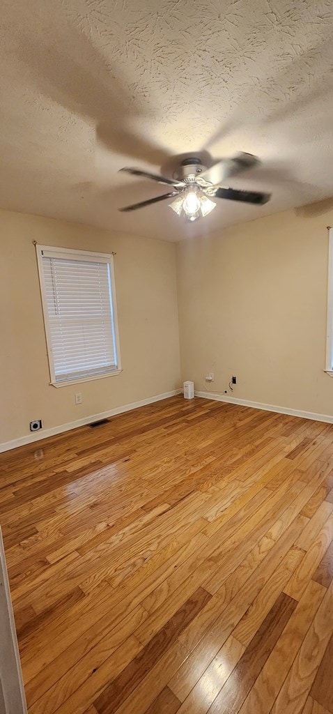 empty room featuring baseboards, visible vents, ceiling fan, a textured ceiling, and light wood-style floors