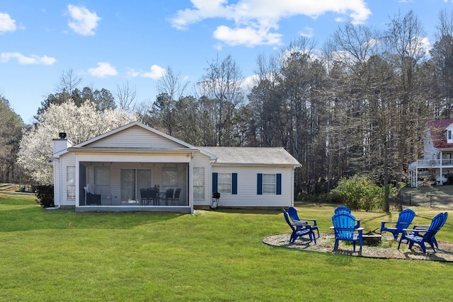 rear view of house with a fire pit, a chimney, a lawn, and a sunroom