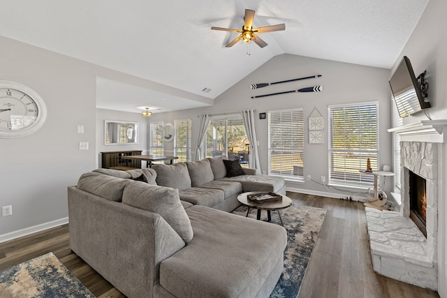 living room with a ceiling fan, baseboards, lofted ceiling, a stone fireplace, and dark wood-type flooring