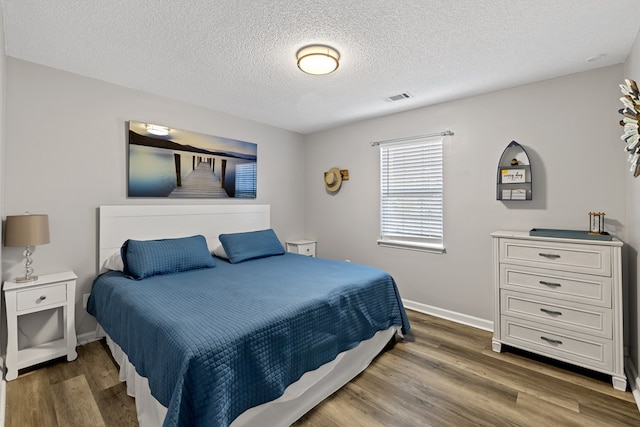 bedroom with visible vents, baseboards, a textured ceiling, and wood finished floors