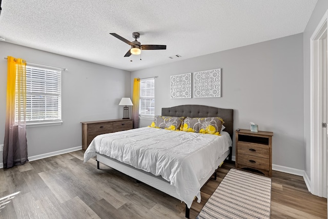 bedroom featuring visible vents, a ceiling fan, a textured ceiling, wood finished floors, and baseboards