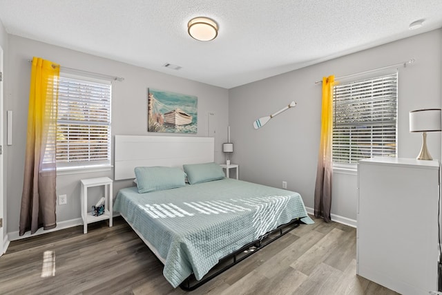 bedroom featuring baseboards, wood finished floors, visible vents, and a textured ceiling