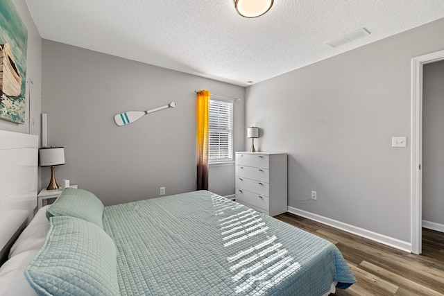 bedroom featuring a textured ceiling, wood finished floors, visible vents, and baseboards