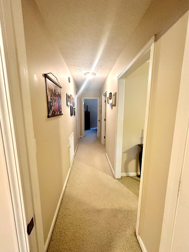 hall with light carpet, a textured ceiling, and baseboards