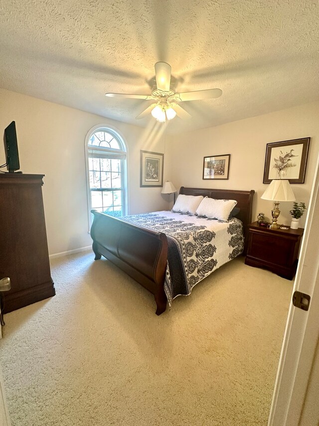 carpeted bedroom with a textured ceiling, a ceiling fan, and baseboards