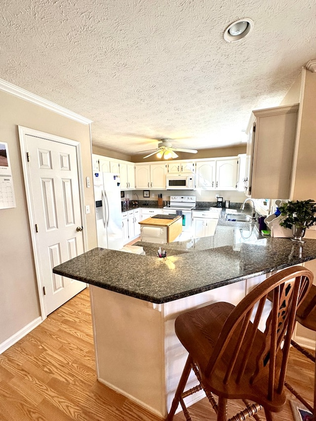 kitchen featuring a breakfast bar area, light wood finished floors, a sink, white appliances, and a peninsula