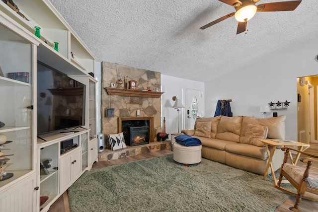 living room with a textured ceiling, vaulted ceiling, ceiling fan, wood-type flooring, and a stone fireplace