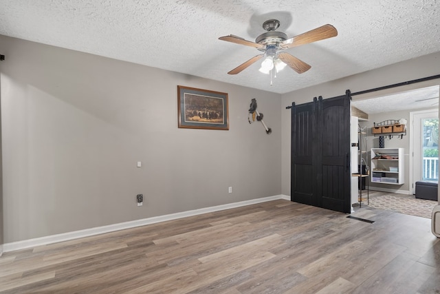 empty room featuring a barn door, ceiling fan, a textured ceiling, and light wood-type flooring