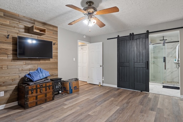 interior space with ceiling fan, a barn door, wood walls, ensuite bathroom, and hardwood / wood-style flooring