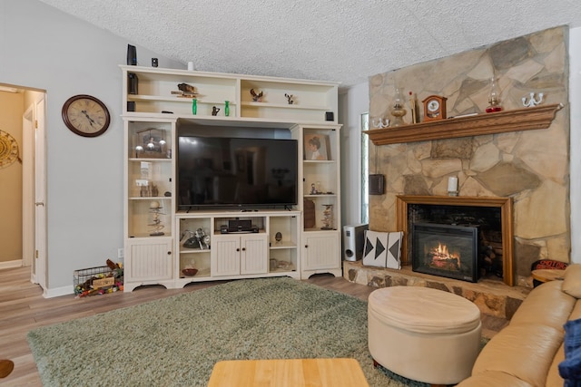 living room featuring a stone fireplace, lofted ceiling, hardwood / wood-style floors, and a textured ceiling