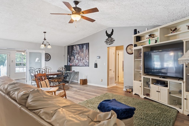 living room with a textured ceiling, ceiling fan with notable chandelier, light hardwood / wood-style flooring, and vaulted ceiling