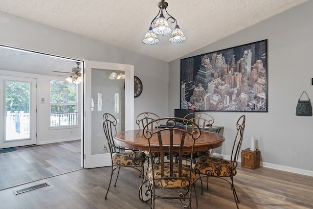 dining space with a textured ceiling, ceiling fan with notable chandelier, hardwood / wood-style flooring, and vaulted ceiling