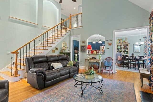 living room with hardwood / wood-style floors, ceiling fan with notable chandelier, crown molding, and a high ceiling