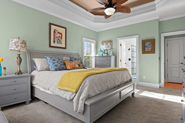 carpeted bedroom with ceiling fan, ornamental molding, ensuite bathroom, and a tray ceiling