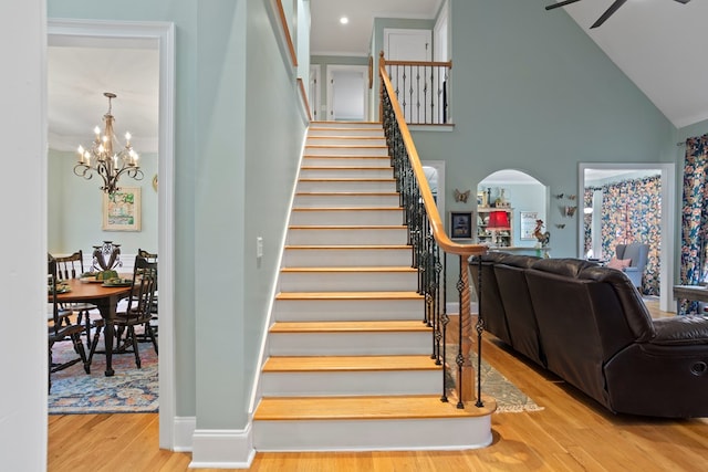 stairs featuring wood-type flooring, ceiling fan with notable chandelier, and high vaulted ceiling