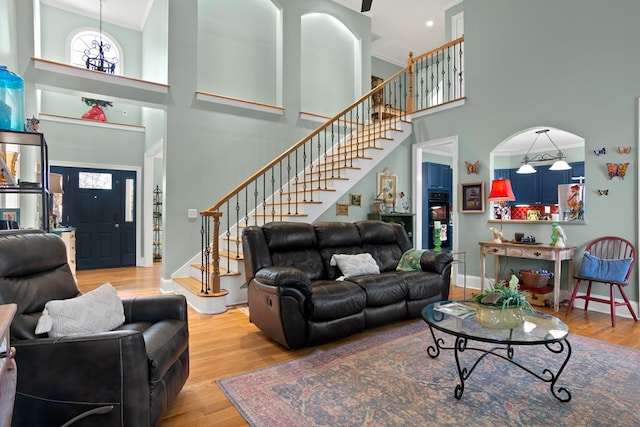 living room featuring light wood-type flooring, a towering ceiling, and crown molding