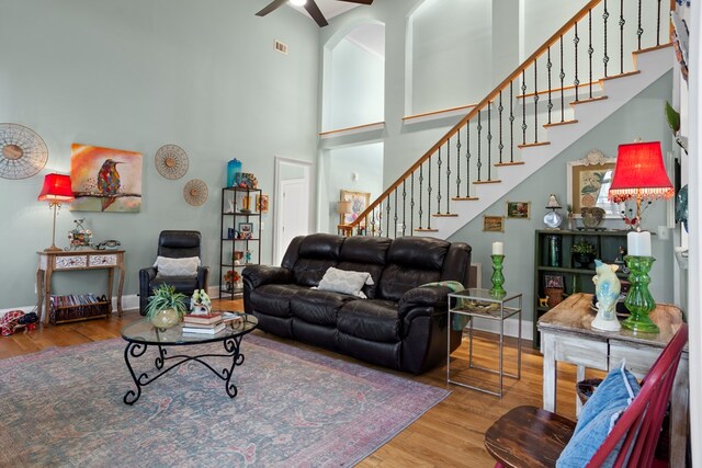 living room with ceiling fan, a towering ceiling, and hardwood / wood-style flooring