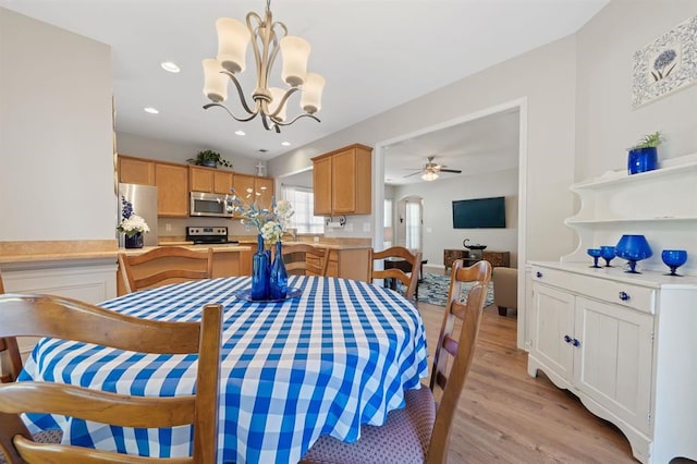 dining area with ceiling fan with notable chandelier and light hardwood / wood-style flooring