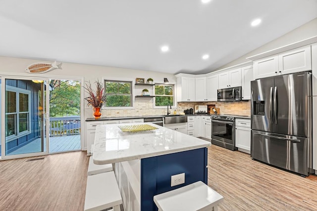 kitchen featuring lofted ceiling, a kitchen island, white cabinets, appliances with stainless steel finishes, and tasteful backsplash