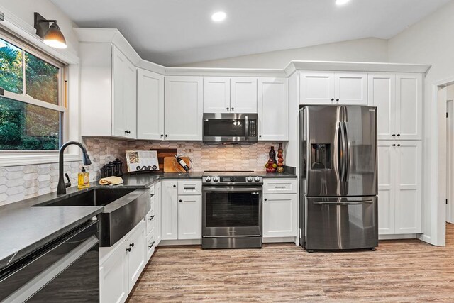 kitchen featuring lofted ceiling, decorative backsplash, white cabinetry, and appliances with stainless steel finishes