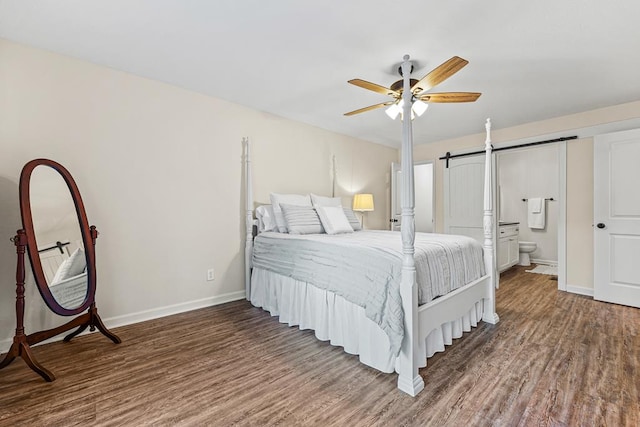 bedroom featuring a barn door, baseboards, dark wood-style floors, ceiling fan, and ensuite bathroom