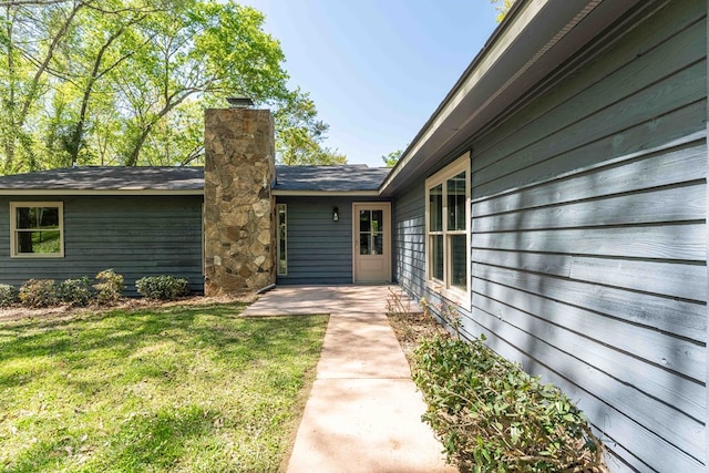 entrance to property featuring a patio area, a chimney, and a yard