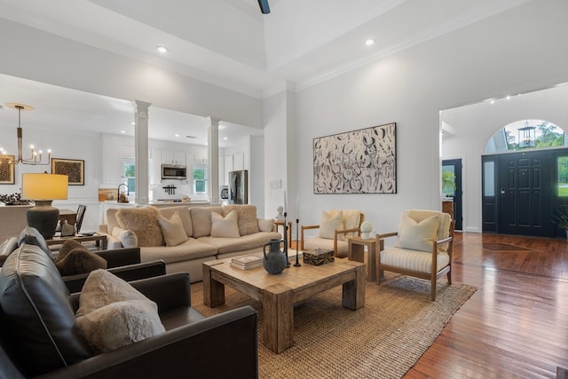 living room featuring hardwood / wood-style floors, a high ceiling, an inviting chandelier, ornamental molding, and decorative columns