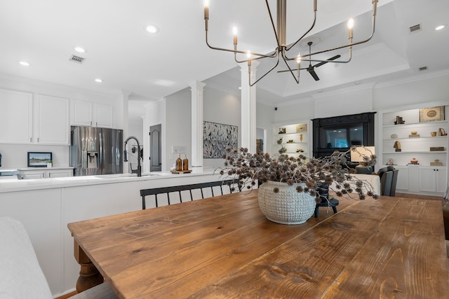 dining space with a raised ceiling, sink, built in features, ornamental molding, and ornate columns