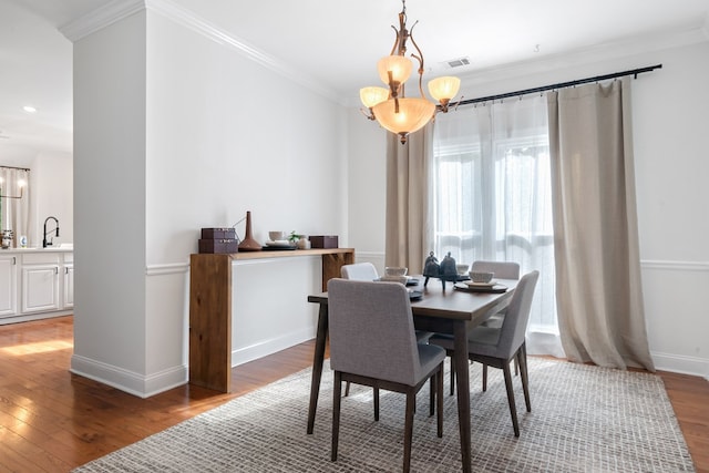 dining area with sink, an inviting chandelier, dark wood-type flooring, and crown molding