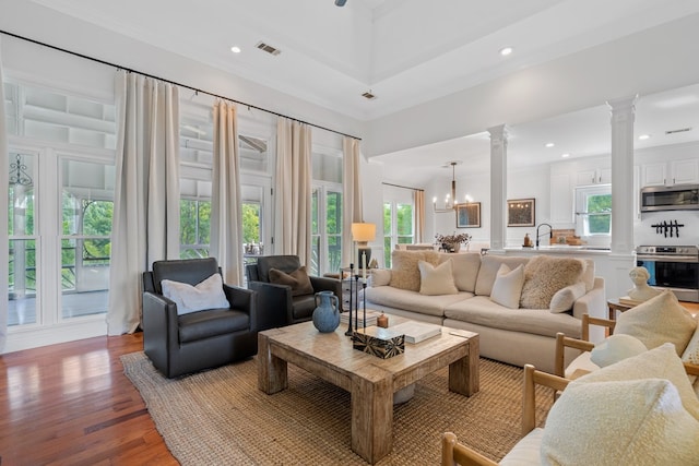 living room featuring ornate columns, ornamental molding, wood-type flooring, an inviting chandelier, and a high ceiling