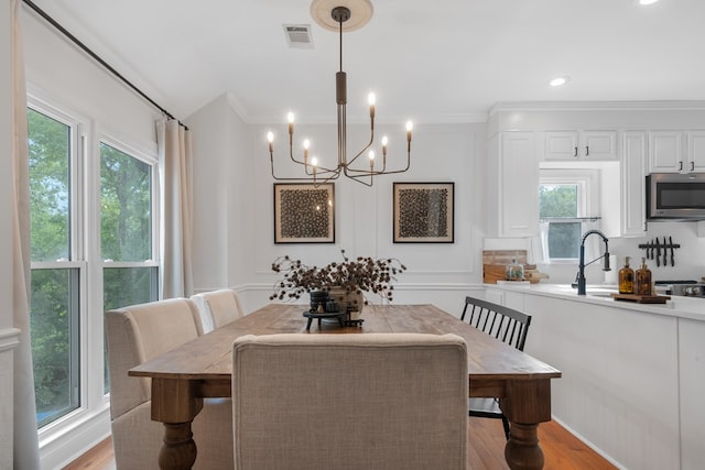 dining room with a wealth of natural light, crown molding, a notable chandelier, and light wood-type flooring