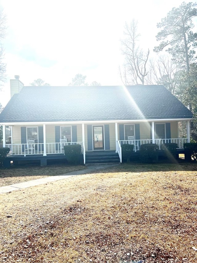 view of front of home featuring roof with shingles, a porch, and a chimney