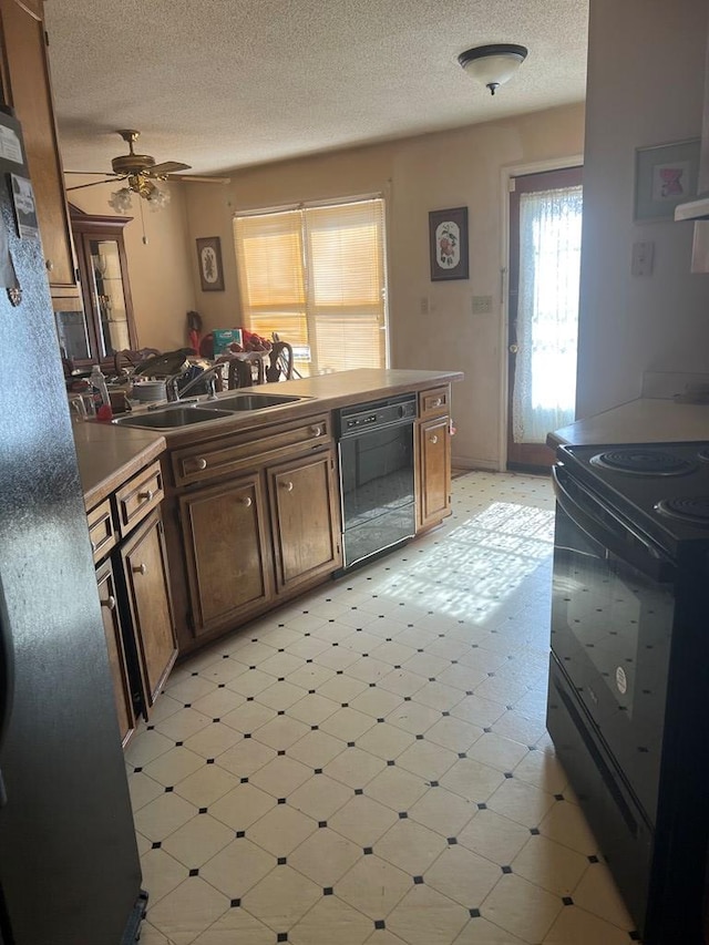 kitchen featuring a textured ceiling, light floors, a sink, light countertops, and black appliances