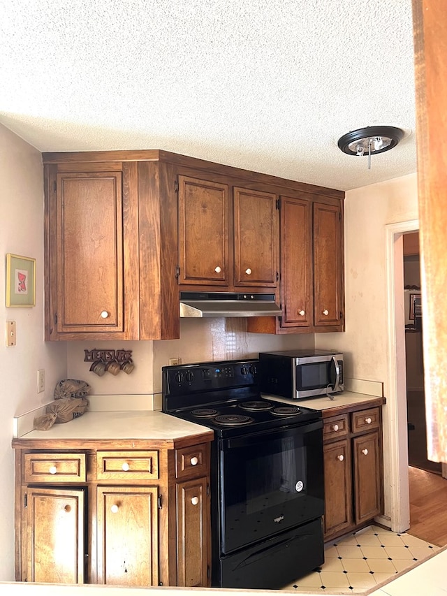 kitchen with stainless steel microwave, light countertops, a textured ceiling, black electric range, and under cabinet range hood