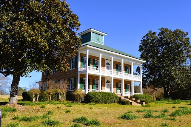 greek revival house featuring a porch, a balcony, and a front lawn