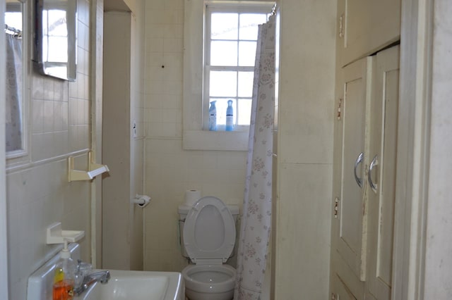 bathroom featuring walk in shower, sink, tile walls, and toilet