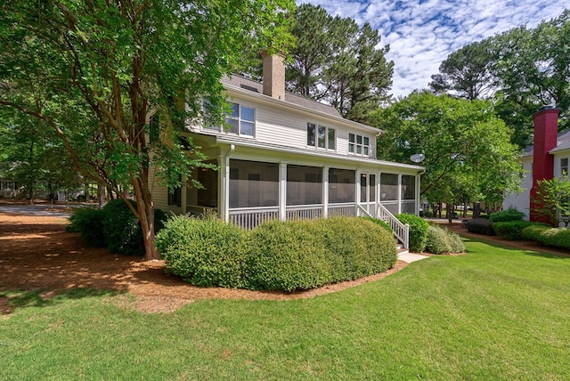 rear view of house featuring a sunroom, a yard, and a chimney