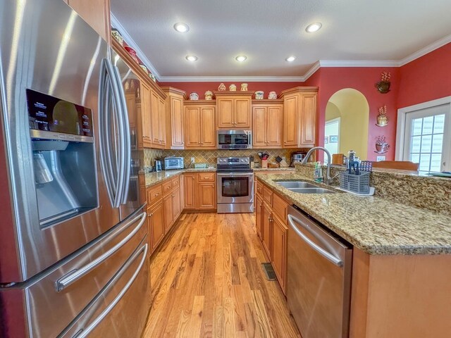 kitchen featuring appliances with stainless steel finishes, tasteful backsplash, sink, crown molding, and light hardwood / wood-style flooring