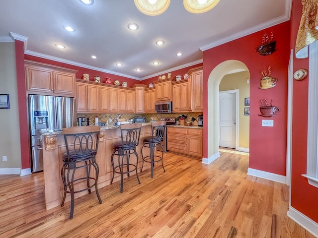 kitchen featuring a breakfast bar, light wood-type flooring, ornamental molding, stainless steel appliances, and backsplash