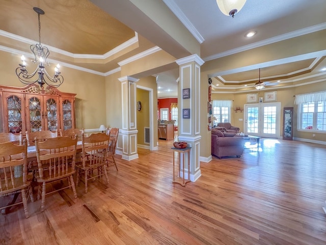 dining space featuring crown molding, light hardwood / wood-style flooring, ceiling fan with notable chandelier, a raised ceiling, and ornate columns