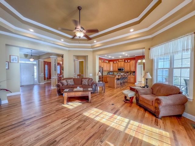 living room with light hardwood / wood-style flooring, ornamental molding, a raised ceiling, and decorative columns