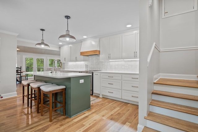 kitchen featuring white cabinets, stainless steel range with electric cooktop, custom exhaust hood, decorative backsplash, and hanging light fixtures