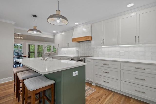 kitchen featuring decorative light fixtures, backsplash, sink, an island with sink, and white cabinets